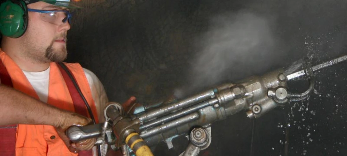 A miner holding hand using a jackhammer with dust in the air