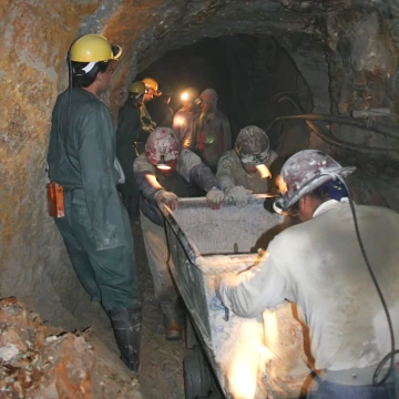 Scene of miners over-exerting themselves pushing ore cars in hot conditions